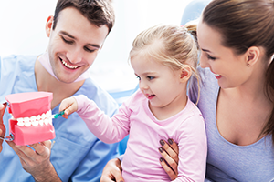 male dentist showing mother and young daughter model of teeth, Pearland, TX family dentistry